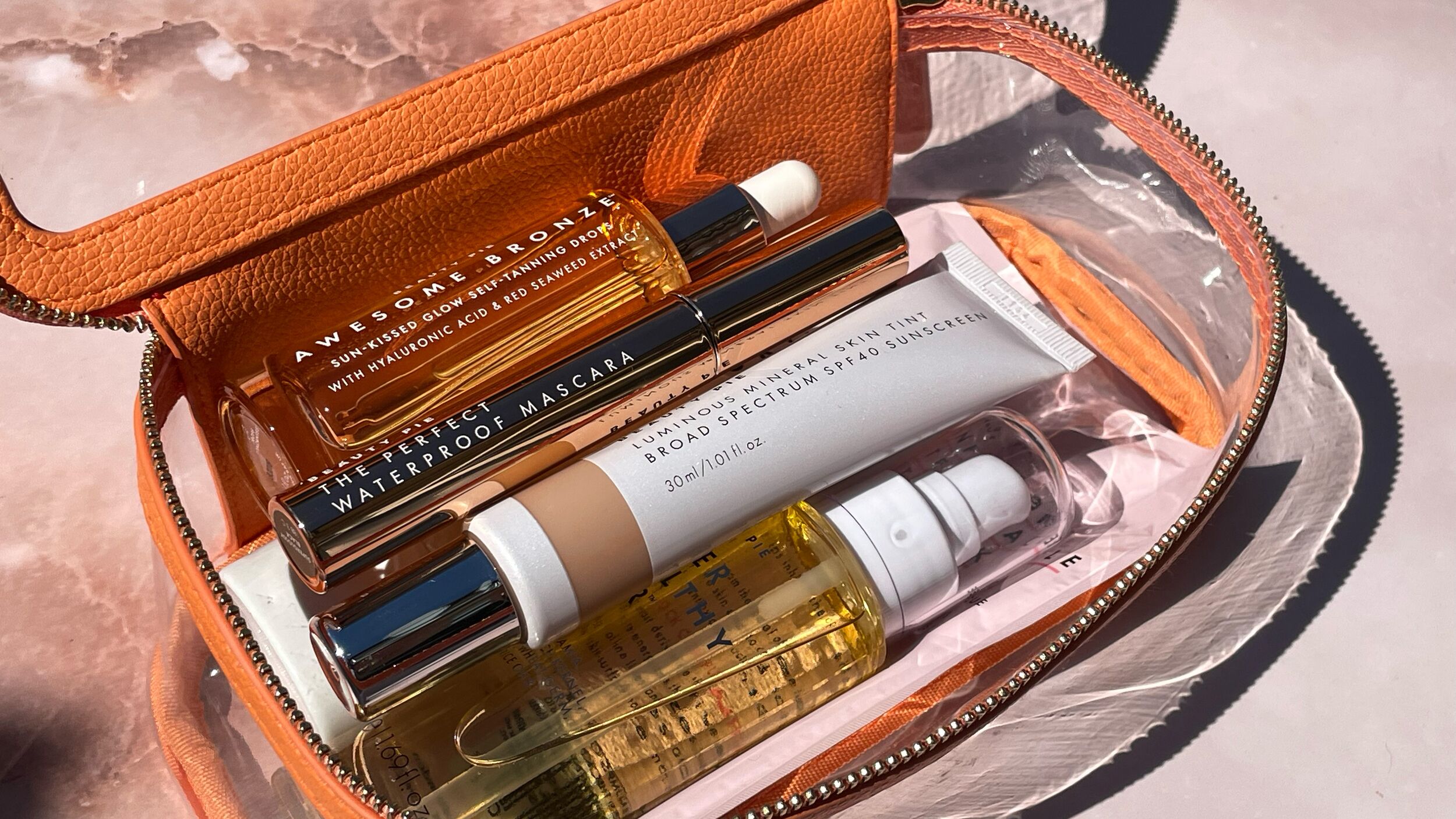 apricot makeup bag filled with Tinted SPF, tanning drops, waterproof mascara